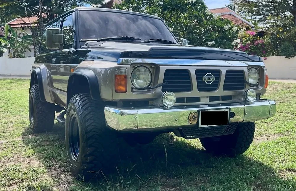 Nissan Patrol Y60 Safari de 1990 negro y gris de batalla corta, en vista tres cuartos delantera en Koh Samui