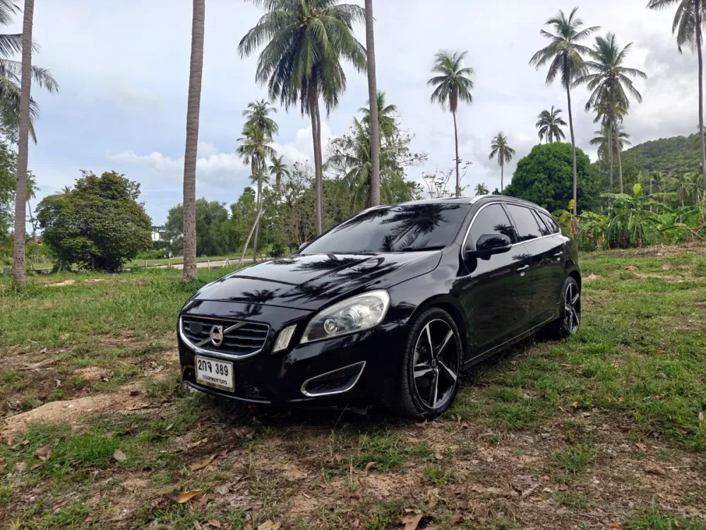 Black Volvo V60 front three-quarter view beneath tropical trees