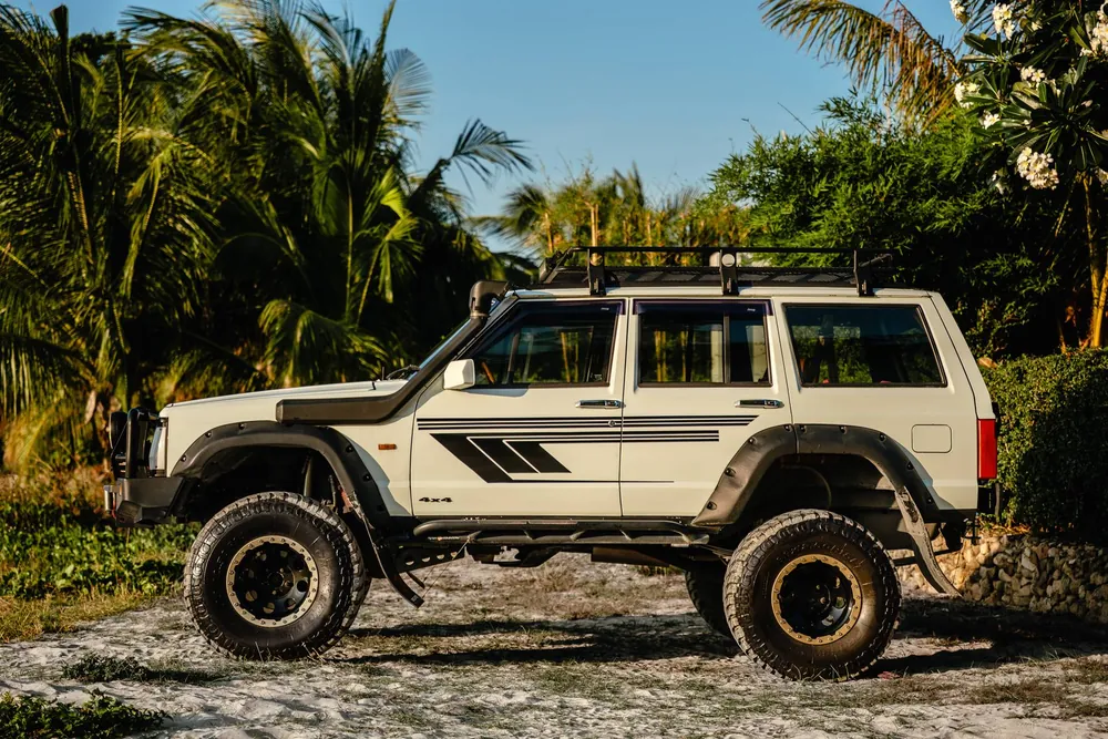 White Samurai lifted Jeep in side profile beneath palm trees on Koh Samui
